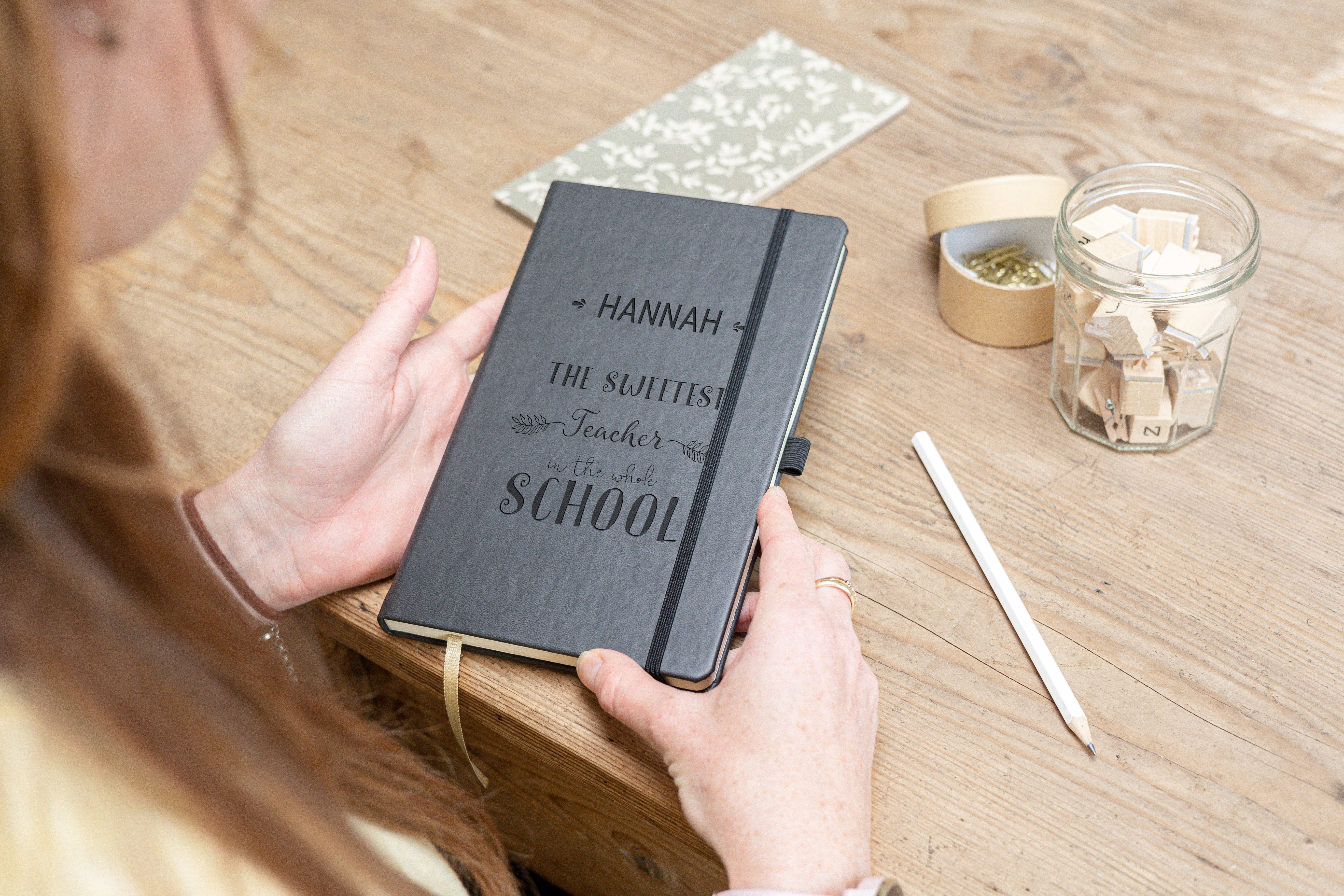 Personalisierte Notizbücher, schwarzes Hardcover, mit dem gravierten Text "Hannah, the sweetest teacher in the whole school", individuell gestaltbar als Geschenk.