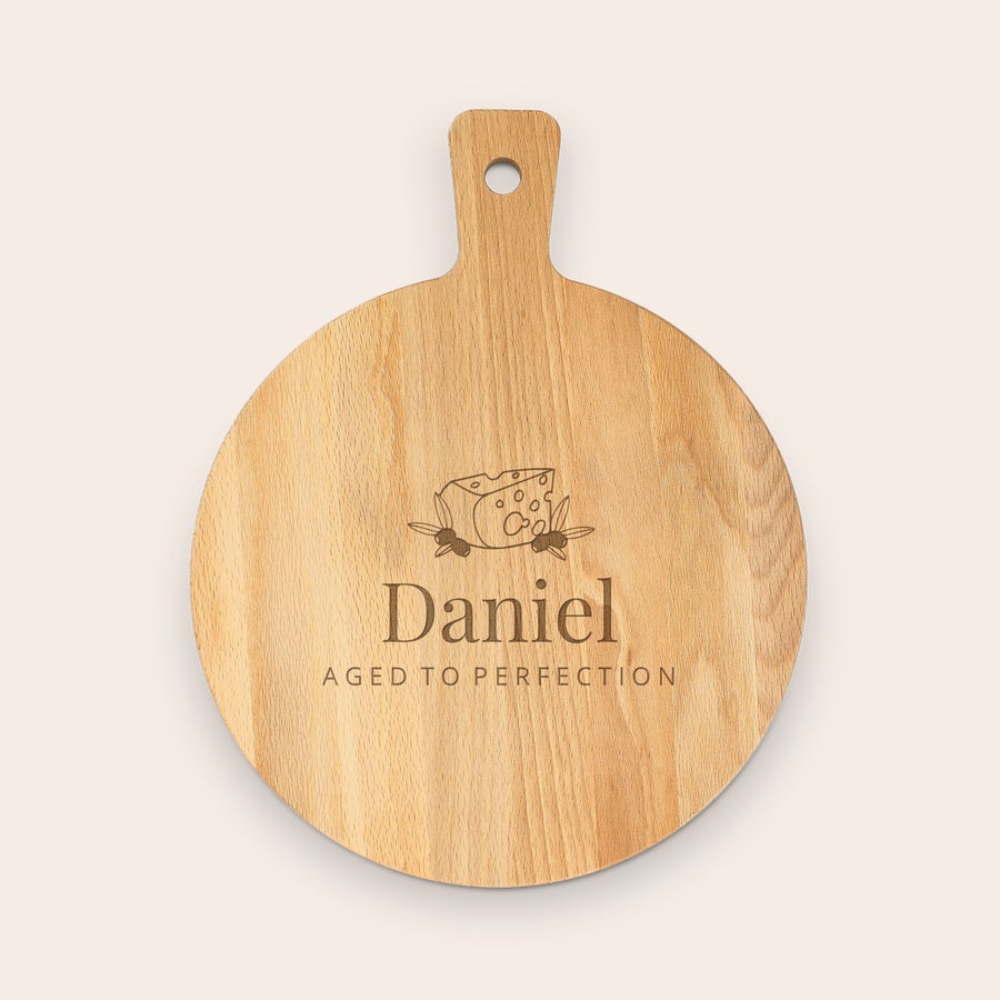 Servírovací podnos na občerstvenie Servírovací podnos z dreva, okrúhly s rúčkou, s gravírovaným nápisom Daniel a Aged to Perfection, v hornej časti syr s olivami.
