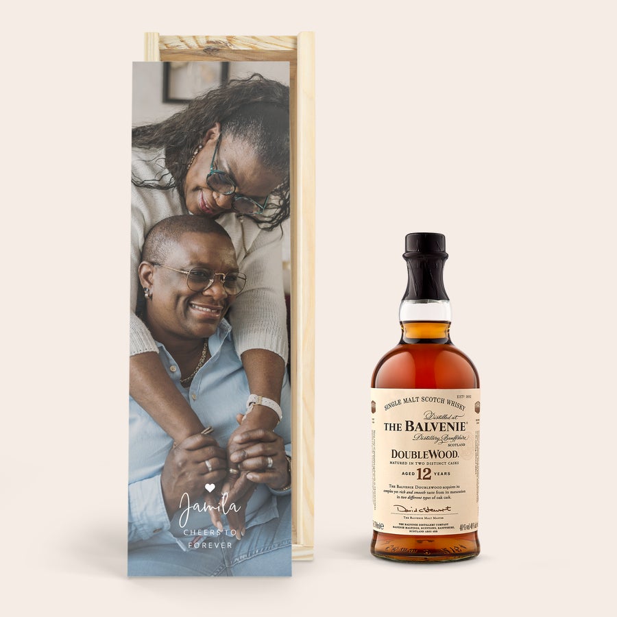 Uísque The Balvenie - Caixa Personalizada Uma linda garrafa de uísque The Balvenie ao lado de uma caixa de madeira personalizada com uma foto impressa de um casal e o texto "Jamila Cheers to Forever".