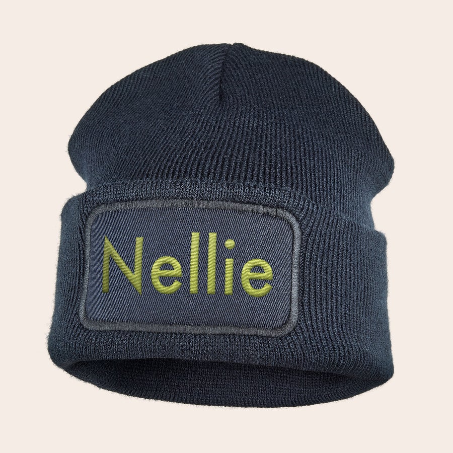 Broderad hatt Mörkblå mössa med namn Nelly broderat i gul text på en personlig patch. Håll dig varm med en personaliserad mössa.