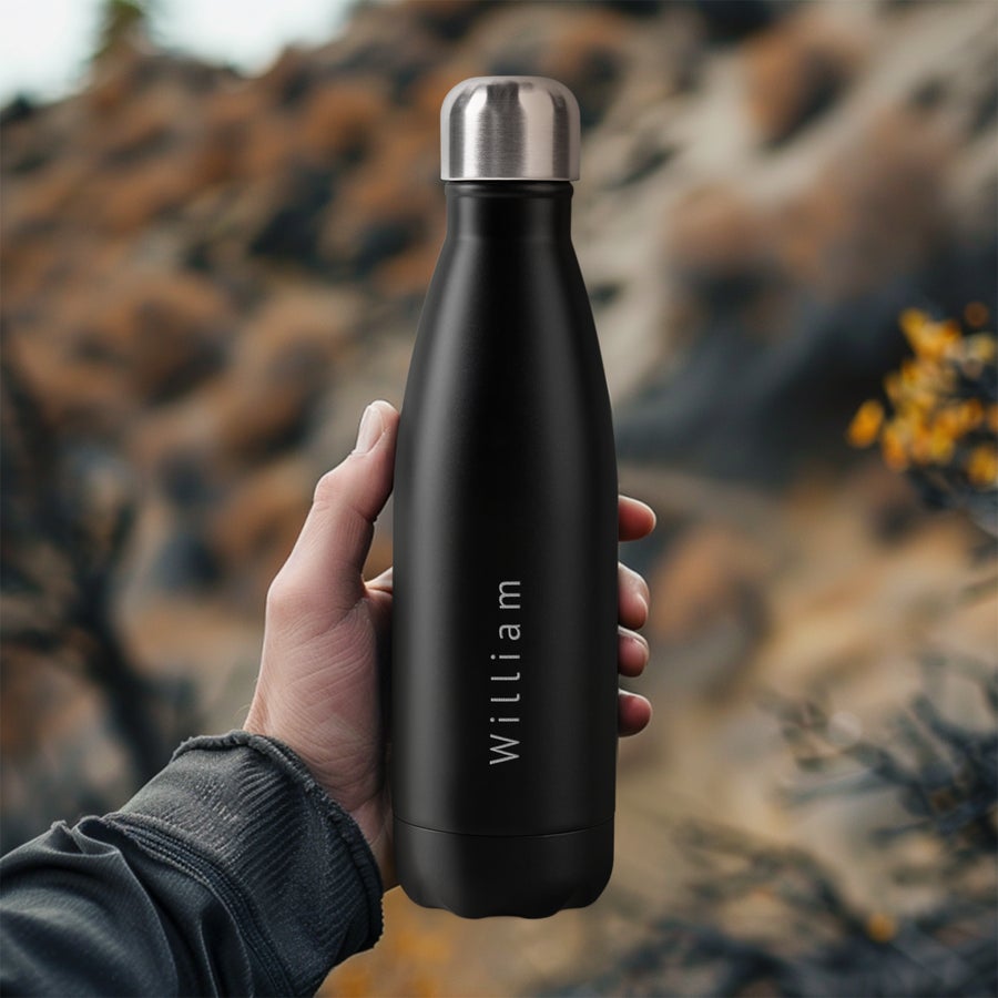 Termoska - gravírovaná Ruka drží čiernu termosku s vygravírovaným menom William. Personalizovaná termoska na cesty.