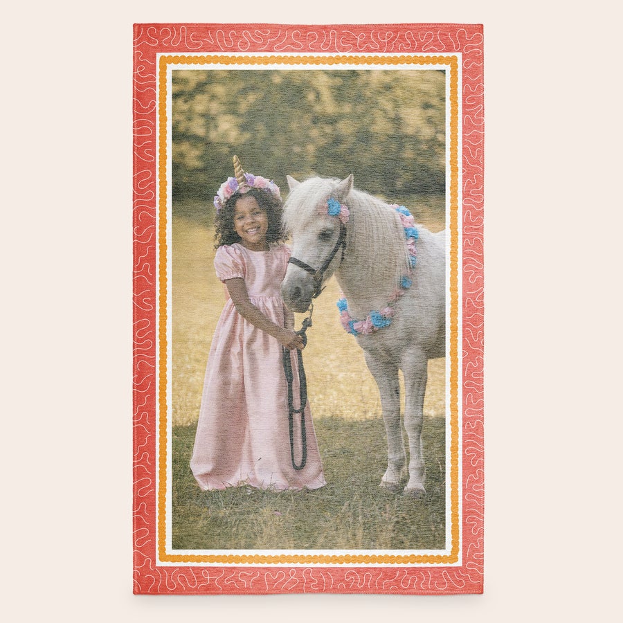 Natisnjena igralna podloga Personalizirana igralna podloga z natisnjeno fotografijo deklice in ponija, obrobljena z rdečim vzorcem.