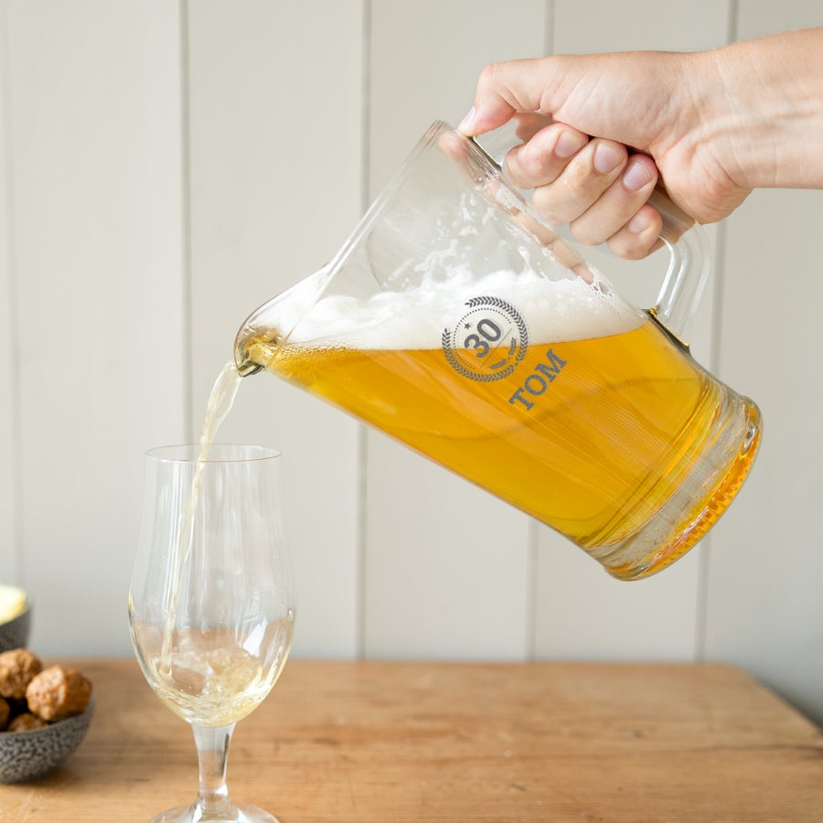 Glaskrug mit Gravur Glaskrug mit Gravur "30 TOM" gefüllt mit Bier wird in ein Glas gegossen, ideal für Text deiner Wahl.