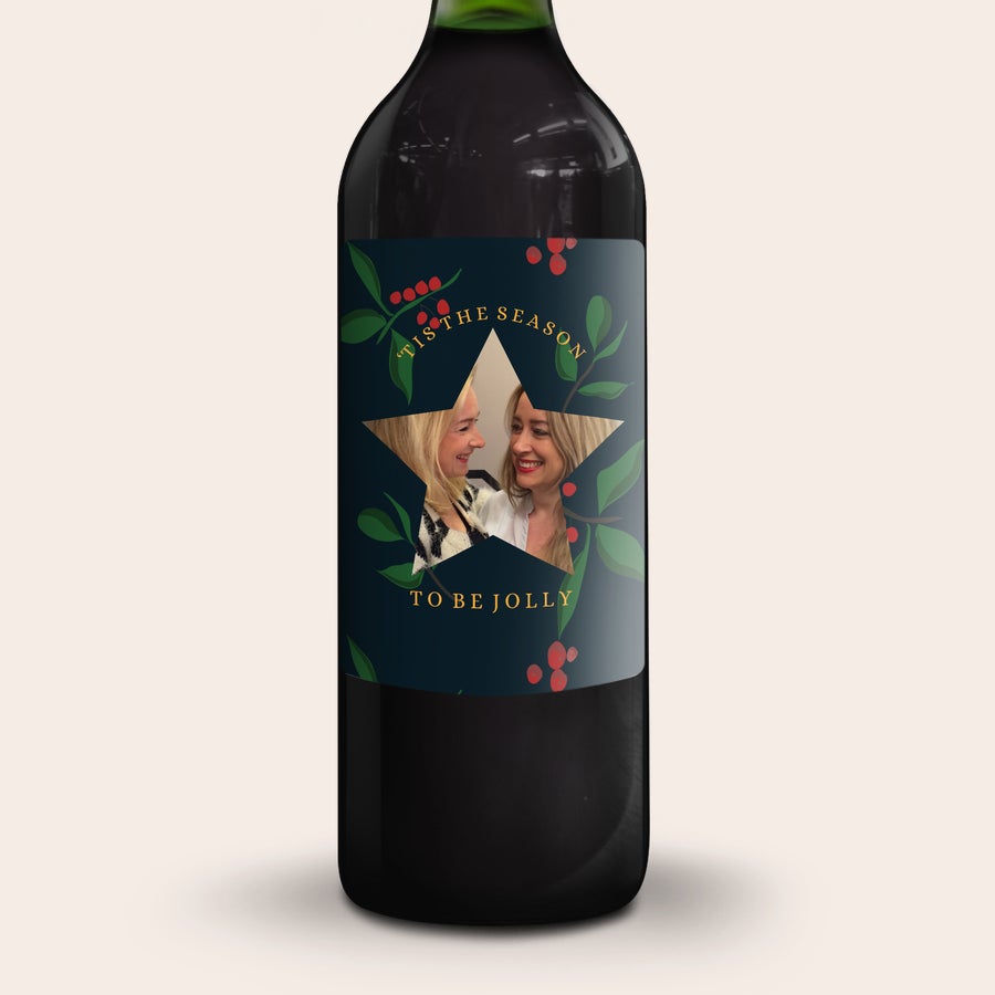 Gluhwein Engelsglut Botella de glühwein personalizada con foto de dos mujeres en una etiqueta temática de Navidad con el texto 'Tis the season to be jolly'.