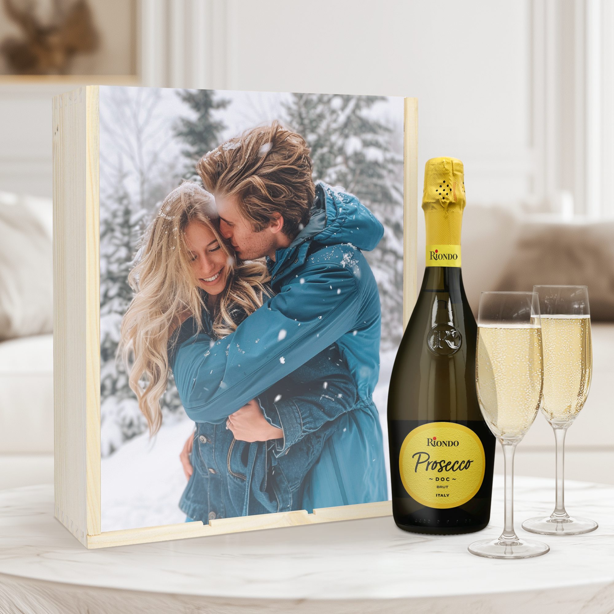 Caja de madera con foto impresa de pareja nevando, botella de Riondo Prosecco y dos copas de champán.
