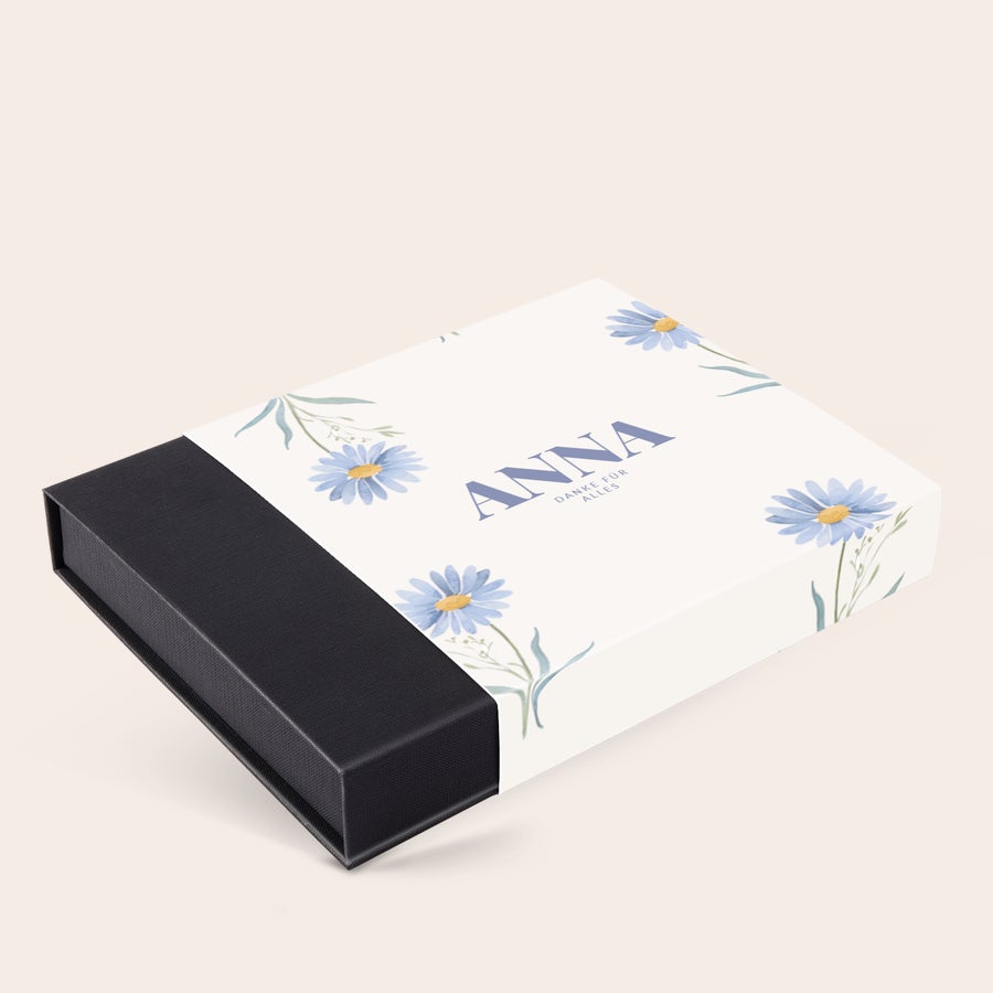 Personalisierte Pralinen Weiße Pralinenverpackung selbst gestalten – 36 Pralinen mit blauem Gänseblümchen-Design und dem Namen „ANNA“ darauf.