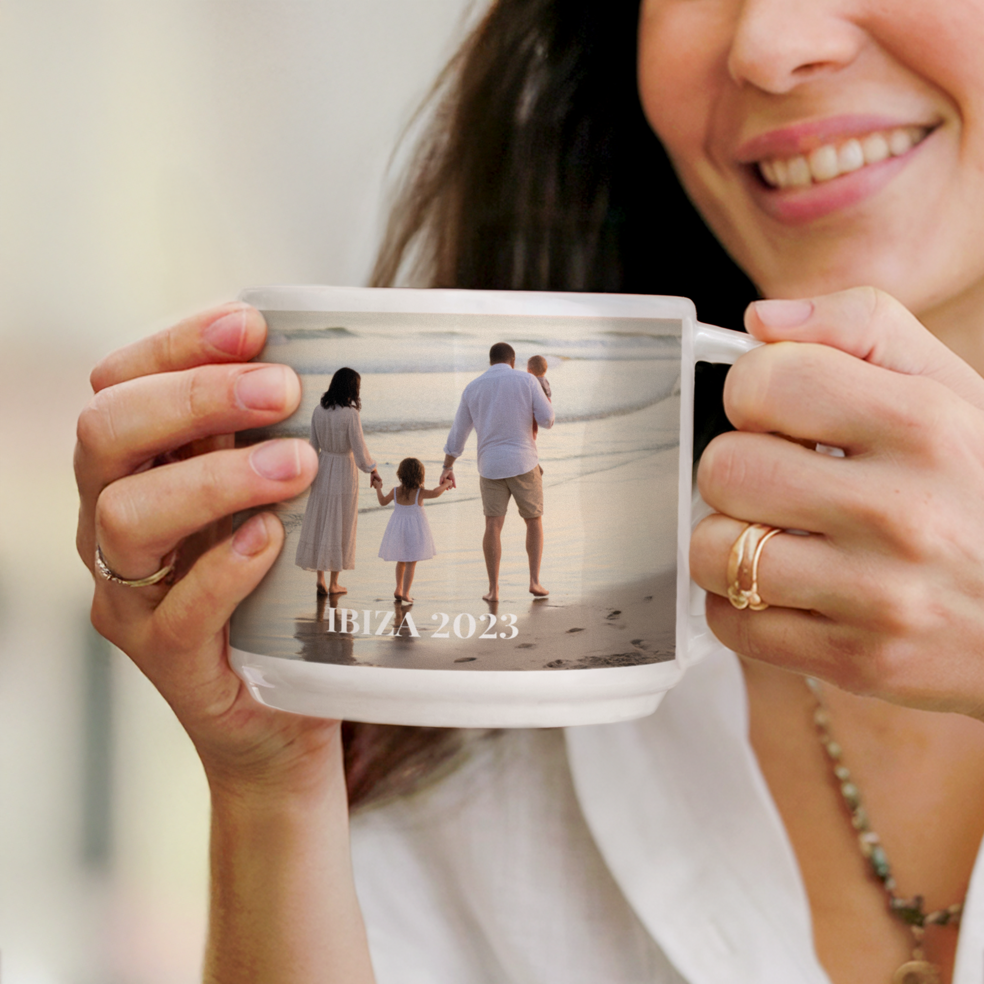 Mujer sonriente sujetando una taza apilable con foto de una familia en la playa y texto "IBIZA 2023"