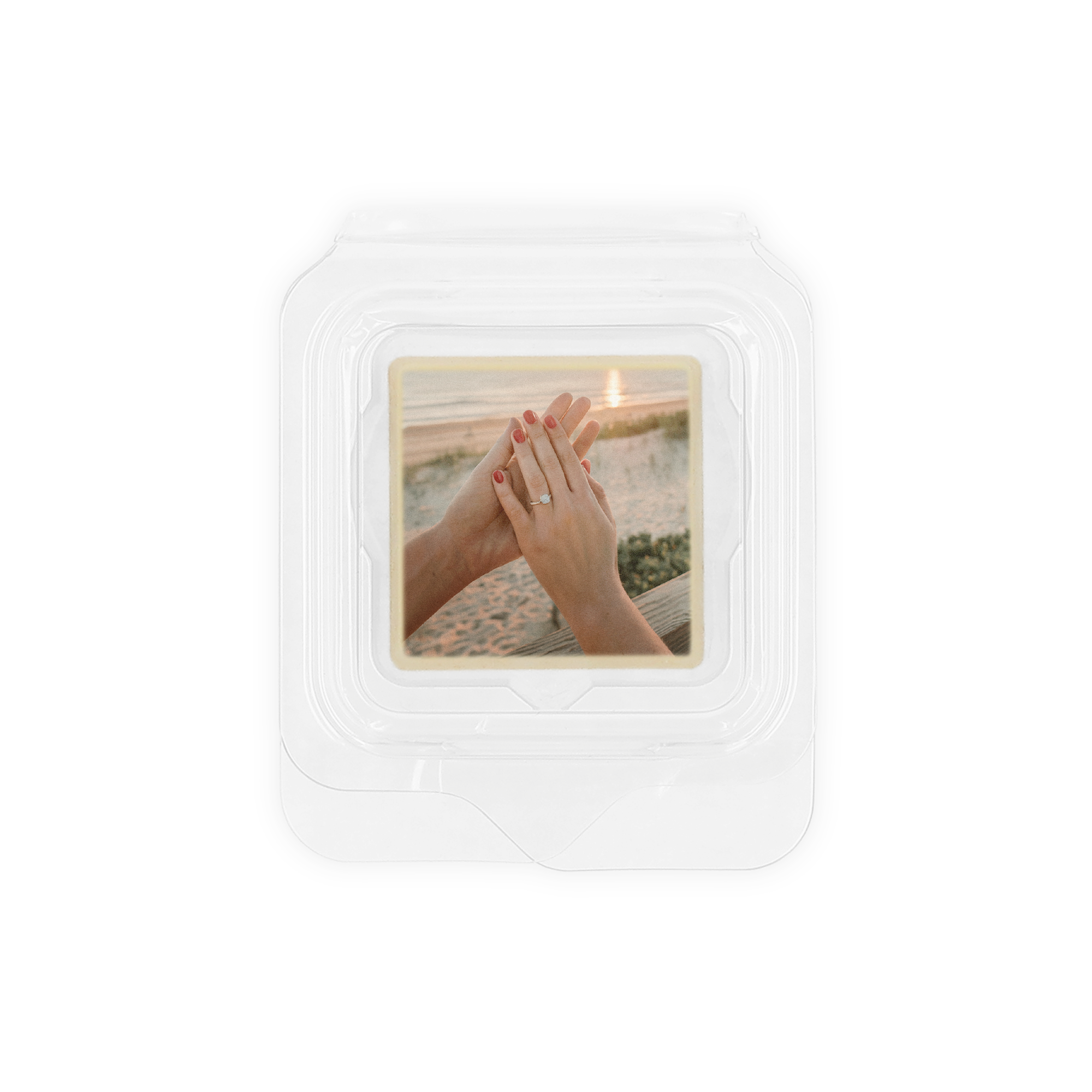 Witte fotopraline met hazelnootpralinévulling, bedrukt met foto van handen en ring voor een strand zonsondergang.