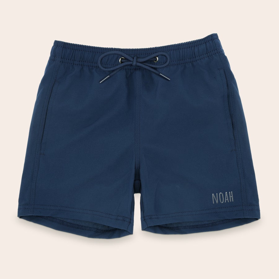 Bañadores personalizados Shorts de baño azules para hombre con el nombre "NOAH" bordado en gris claro en la pierna derecha.