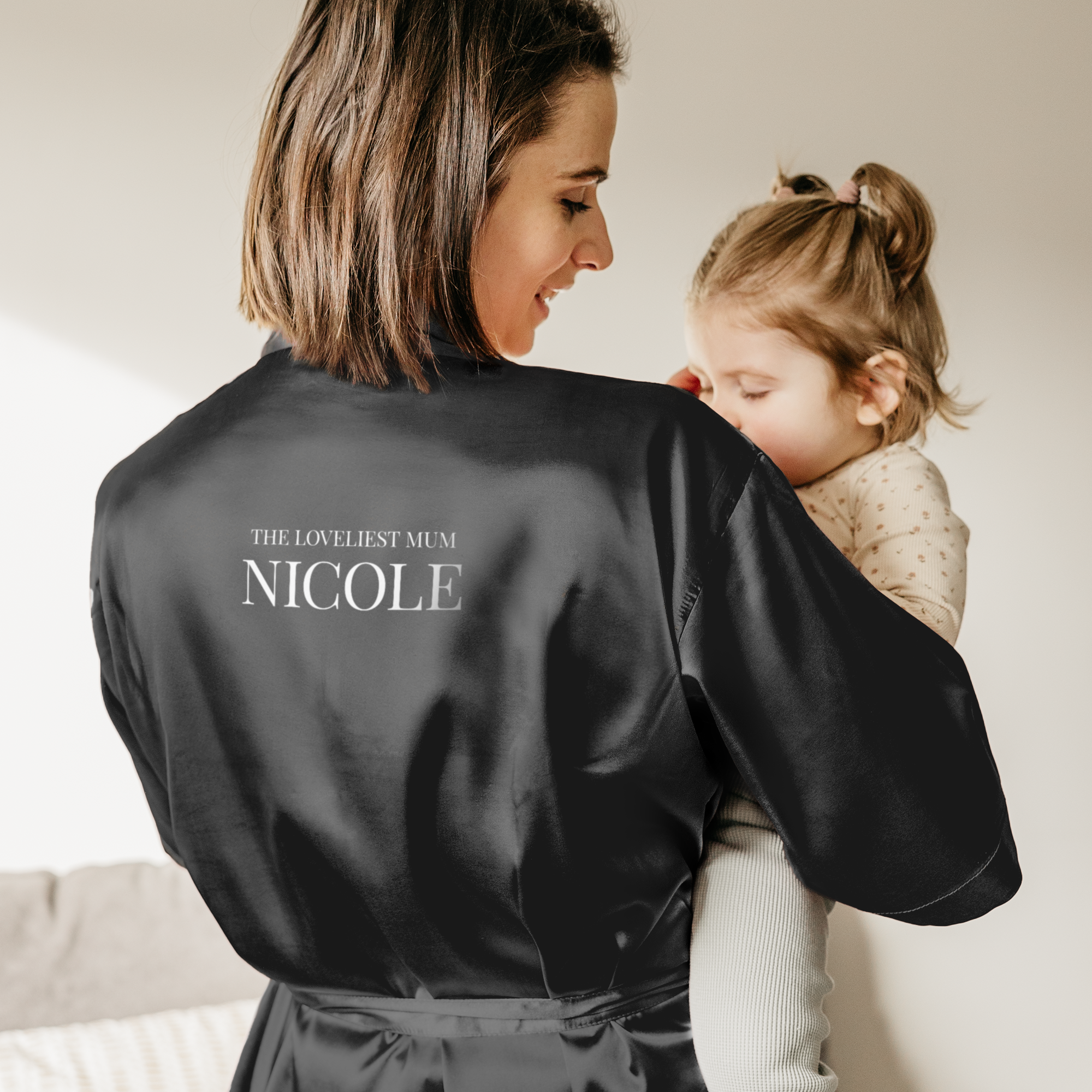 Yksilöllinen kimono mustana, jossa teksti The Loveliest Mum Nicole on painettu selkään, äiti pitelee lasta
