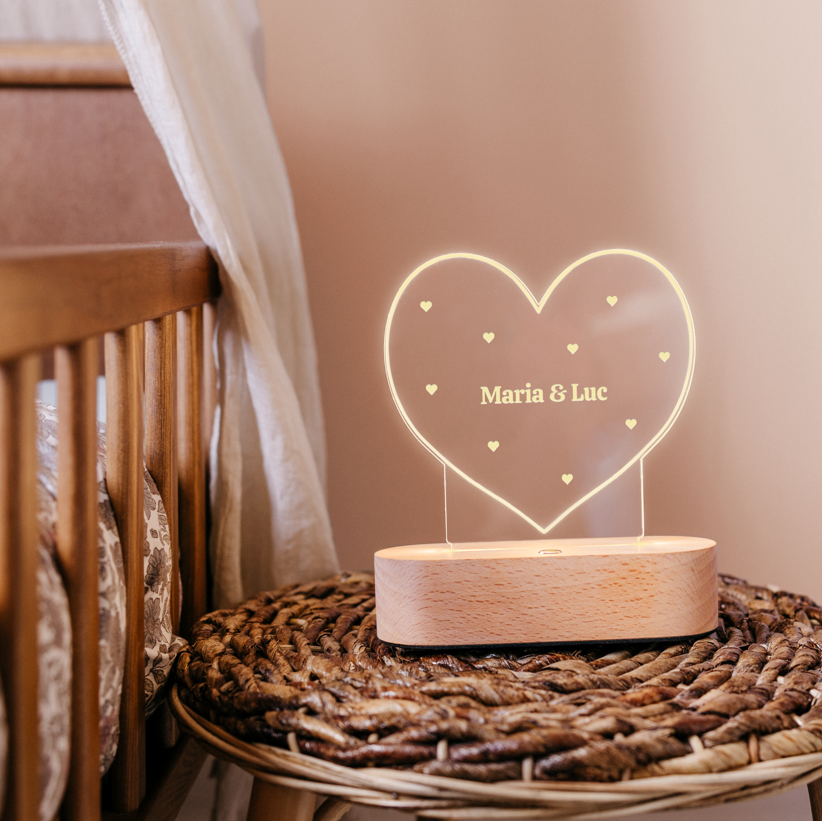 Luz acrílica en forma de corazón con base de madera, grabada con "Maria & Luc" y pequeños corazones.