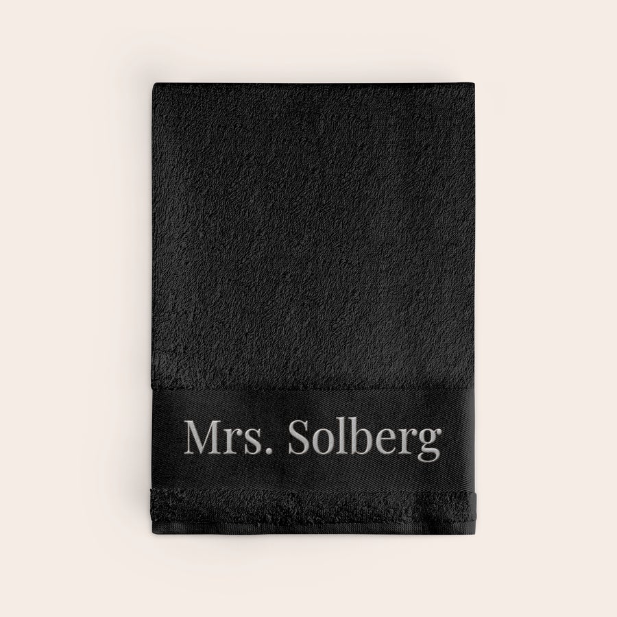 Badehåndkle med tekst Svart personlig badehåndkle brodert med navnet Mrs. Solberg.