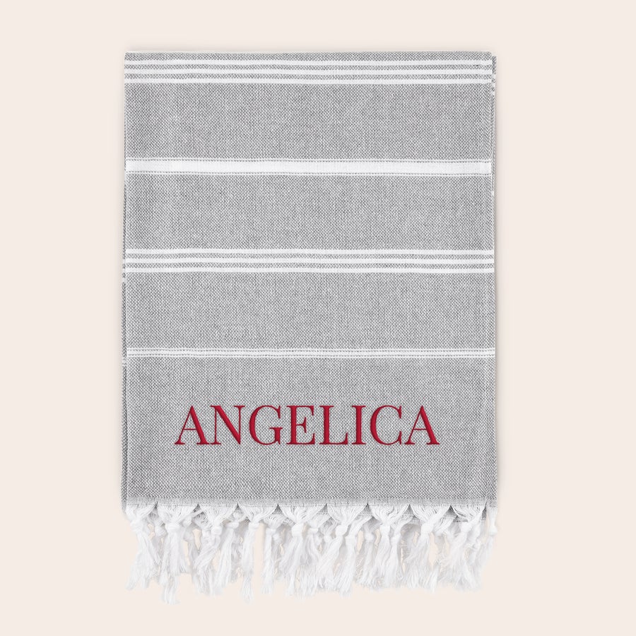 Personlig hammam-handduk Grå och vitrandig hamam-handduk broderad med namnet Angelica i röd tråd, perfekt för att välkomna sommaren med din egen personliga handduk.