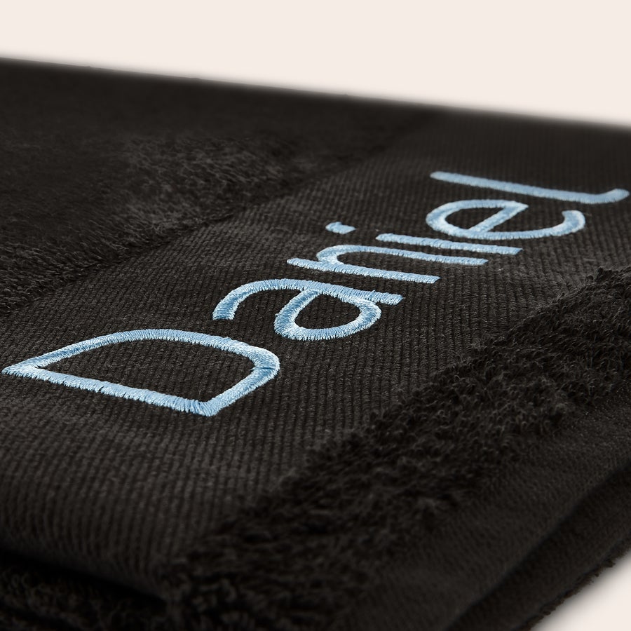 Serviette de bain personnalisée Serviette noire brodée du prénom Daniel en fil bleu clair. Rendez chaque moment du bain unique avec une serviette brodée.