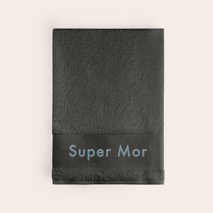 Badehåndklæde med tekst Mørkegråt strand håndklæde broderet med navnet Super Mor i lyseblåt
