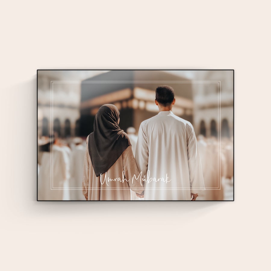 Foto auf Holz Dein Foto gedruckt auf Holz zeigt ein Paar das Händchen haltend vor einem Gebäude steht. Der Schriftzug Umrah Mubarak ist personalisierbar.