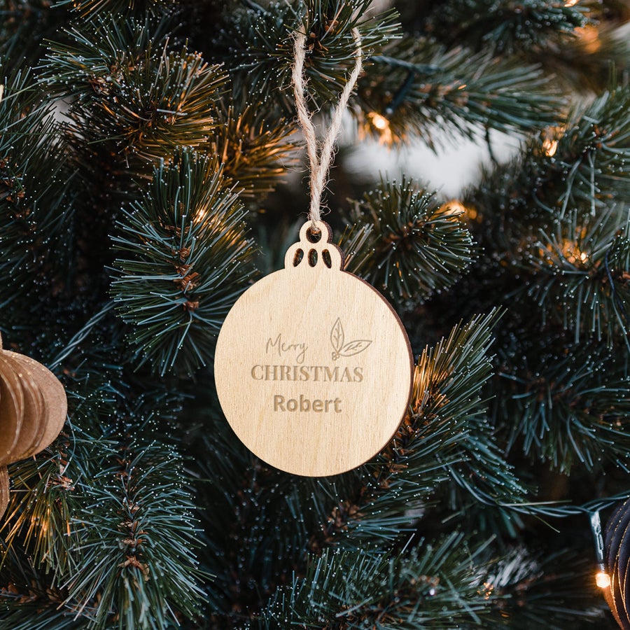 Decorațiune cerc din lemn personalizată cu numele "Robert", gravată cu textul "Merry Christmas" și motive florale, atârnată într-un brad de Crăciun.