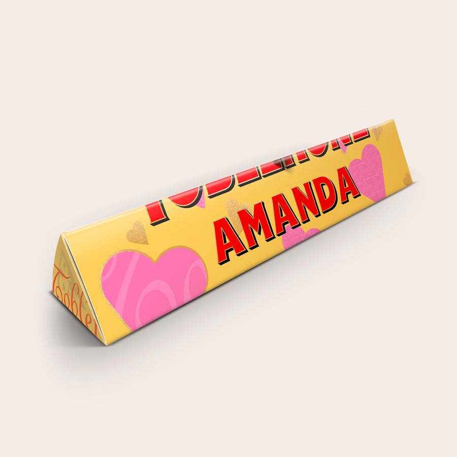Toblerone med namn och foto En personaliserad Toblerone med namn "AMANDA" tryckt i rött på guldfärgad förpackning med hjärtan.