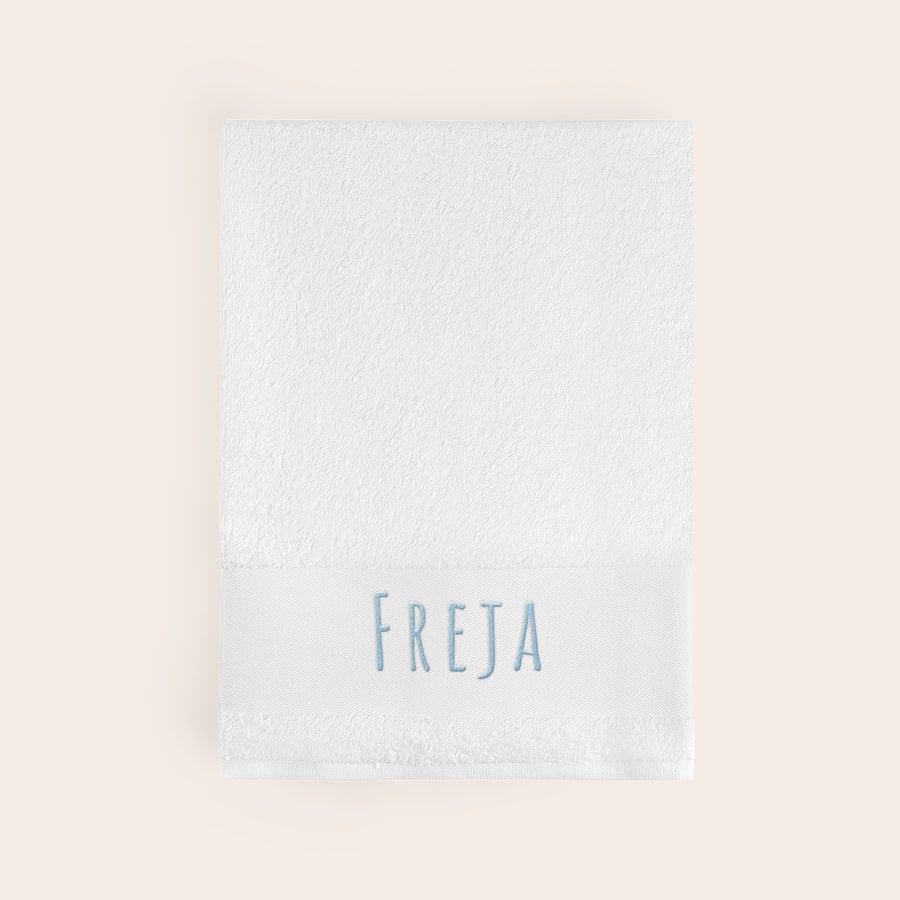 Handduk med Text Vit supermjuk handduk broderad med namnet "FREJA" i ljusblå tråd.