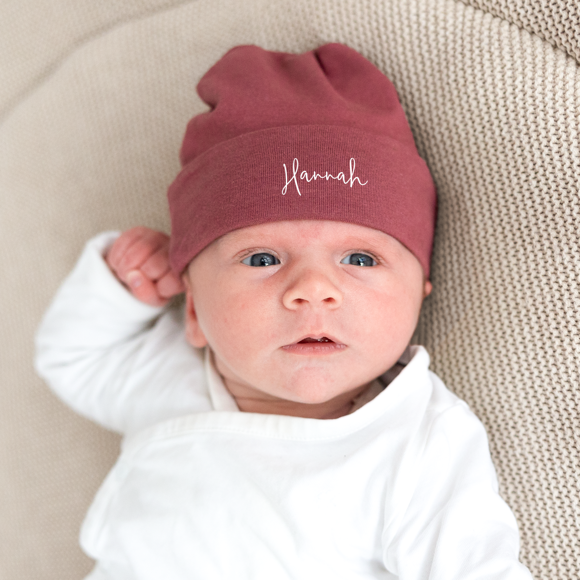 Personalisierte bordeauxrote Babymütze mit Namen Hannah, bedruckt mit weisser Schrift, getragen von einem Baby.