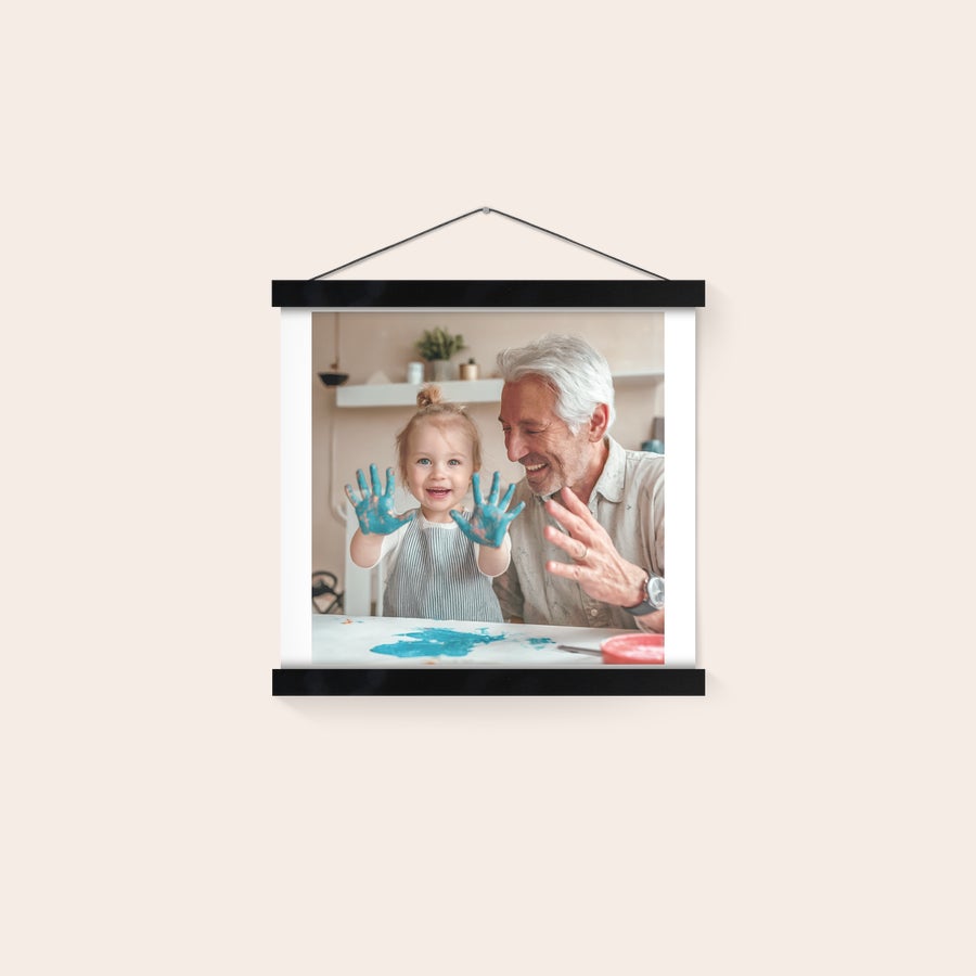 Póster personalizado com suporte Póster personalizado com foto impressa de uma criança e um avô, pendurado num cabide de madeira.