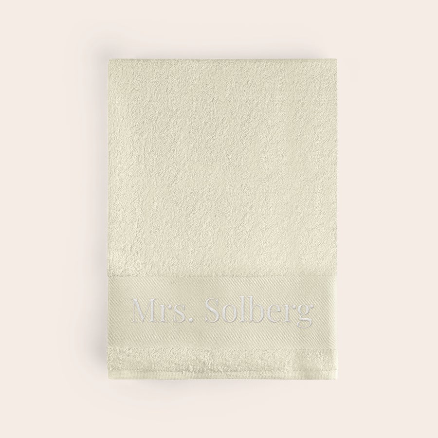Badehåndkle med tekst Beige badehåndkle med navnet Mrs. Solberg brodert i hvitt. Få dette supermyke badehåndkleet brodert med navn!