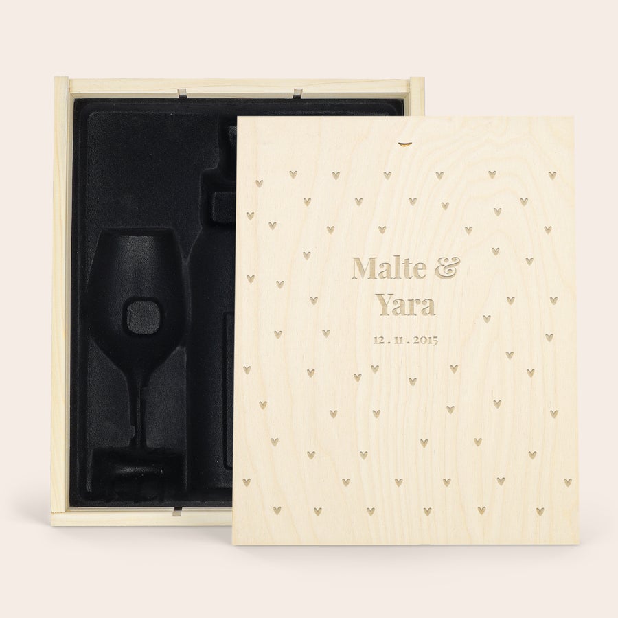 Personalisierte Holzkiste Holzkiste mit persönlicher Gravur von Malte & Yara und dem Datum 12.11.2015, umgeben von Herzen. Innen ist Platz für eine Flasche und zwei Weingläser.