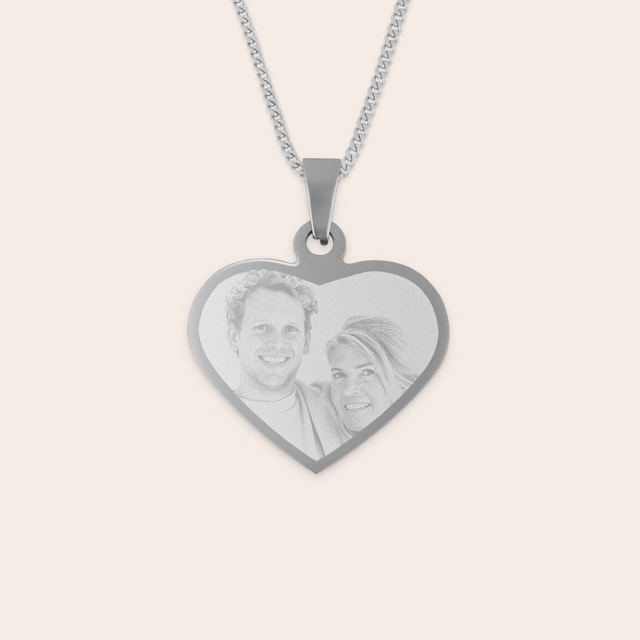 Engraved heart necklace Silver heart-shaped rhodium pendant engraved with a photo of a smiling couple, attached to a metal chain.