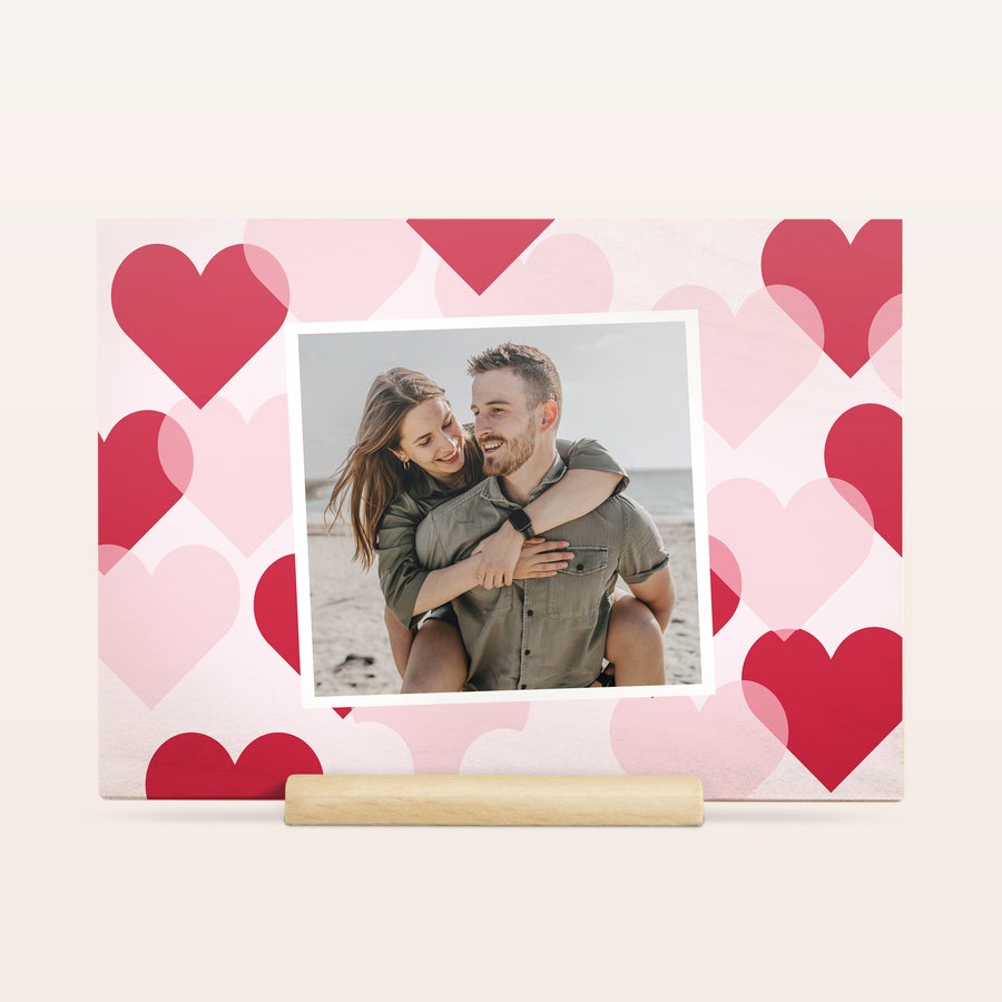 Felicitare Ziua din lemn Îndrăgostiților Carte de lemn de Ziua Îndrăgostiților personalizată cu o fotografie a unui cuplu, imprimată pe un fundal cu inimi roz și roșii.