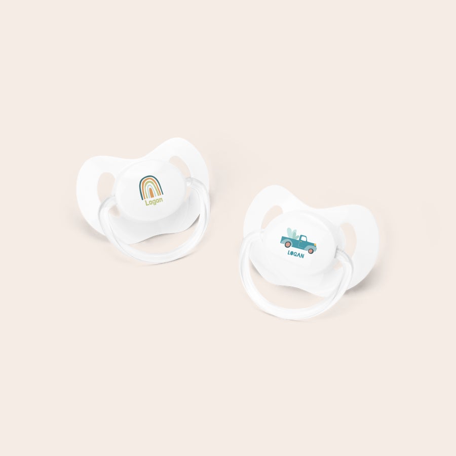 Personalised dummies White personalized dummies with the name Logan printed, one with a rainbow design, the other with a blue truck.