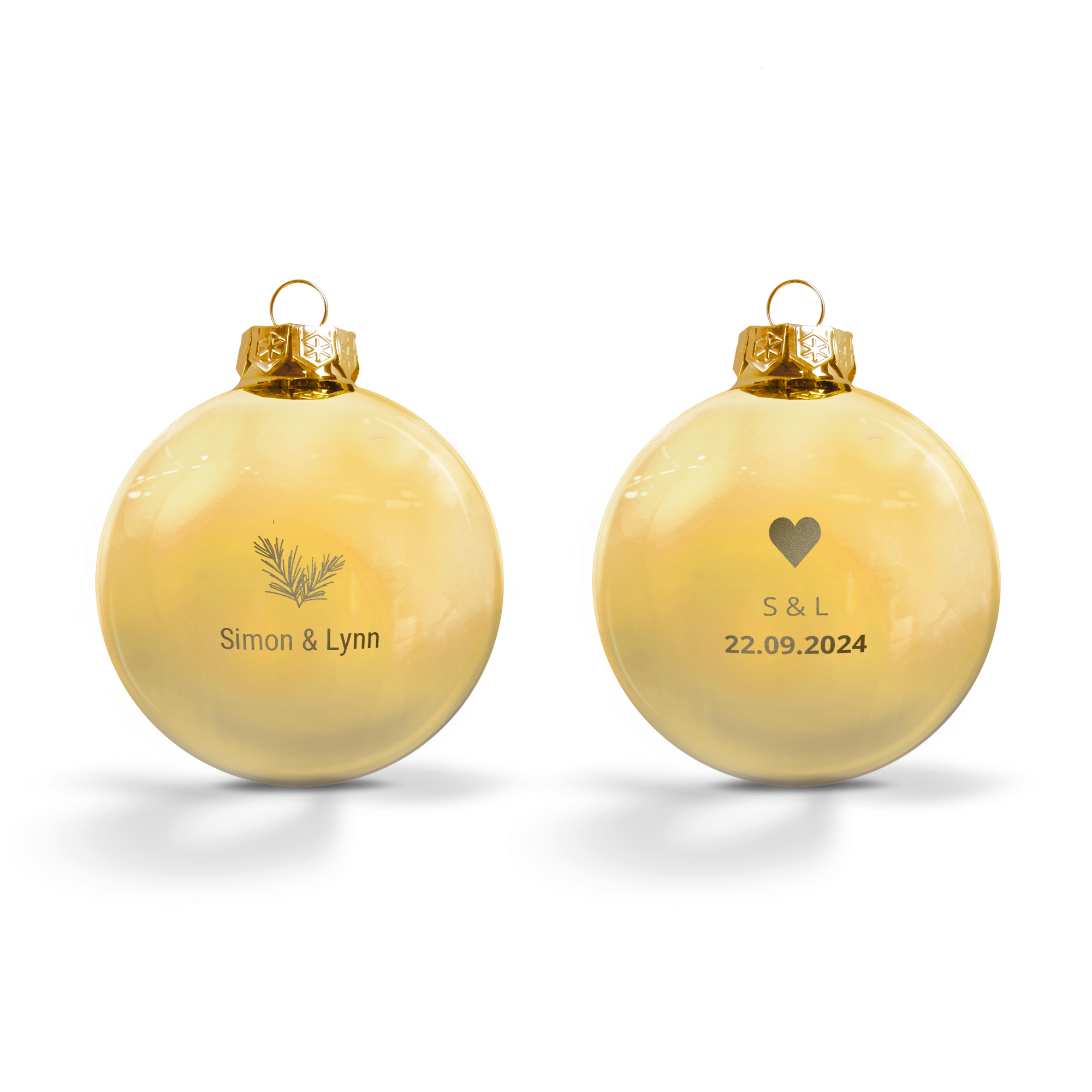 Dos bolas navideñas de cristal grabadas. Una tiene un diseño de ramas de pino y el texto Simon & Lynn. La otra tiene un corazón con S & L y la fecha 22.09.2024. Ambas bolas navideñas tienen una corona dorada.