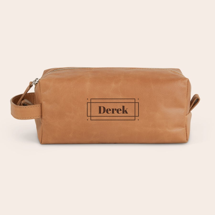 Geantă de toaletă din piele gravată Trusă de toaletă personalizată din piele maro deschis cu fermoar argintiu și mâner lateral, gravată cu numele Derek în stil minimalist. Începe-ți ziua cu stil.