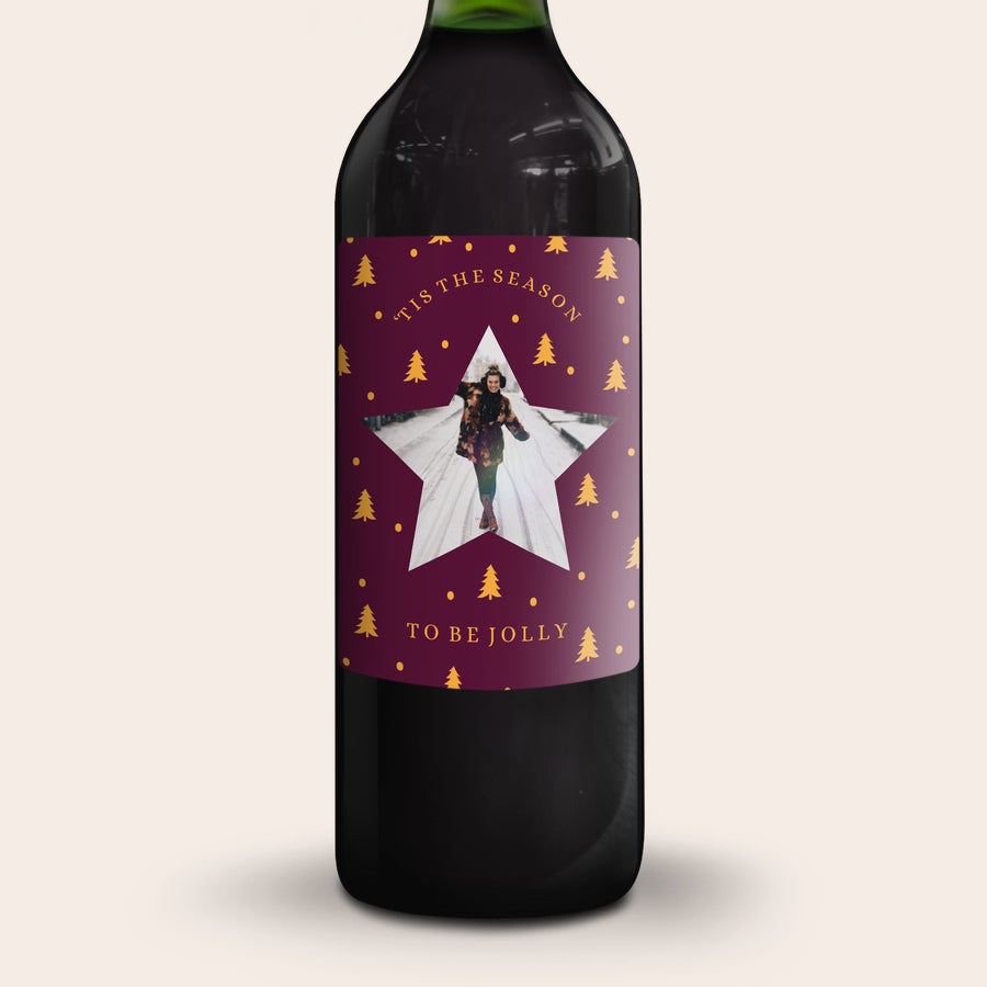 Gluhwein Engelsglut Botella de glühwein con etiqueta personalizada, impresa con una foto festiva y texto "Tis the Season to be Jolly" sobre fondo morado con árboles dorados.