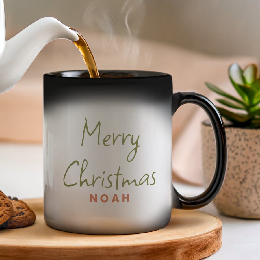 Cană personalizată - Cană magică Cană magică personalizată cu textul Merry Christmas și numele Noah, umplută cu o băutură caldă.