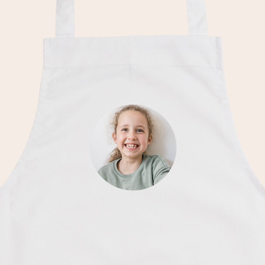 Kinderschürze personalisiert Eine weiße Kinderschürze bedruckt mit dem Foto eines lächelnden Mädchens