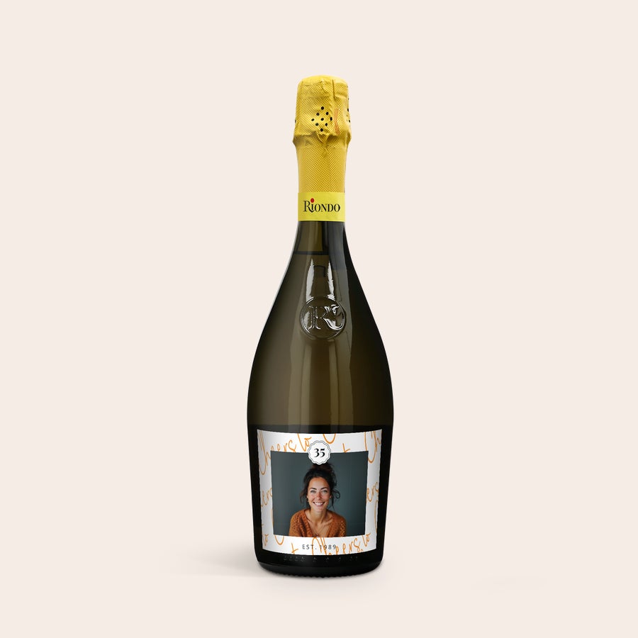 Personlig Riondo Prosecco Spumante En flaska Riondo Prosecco Spumante med en egen etikett där ett foto av en leende kvinna och texten "35 EST. 1989" syns.