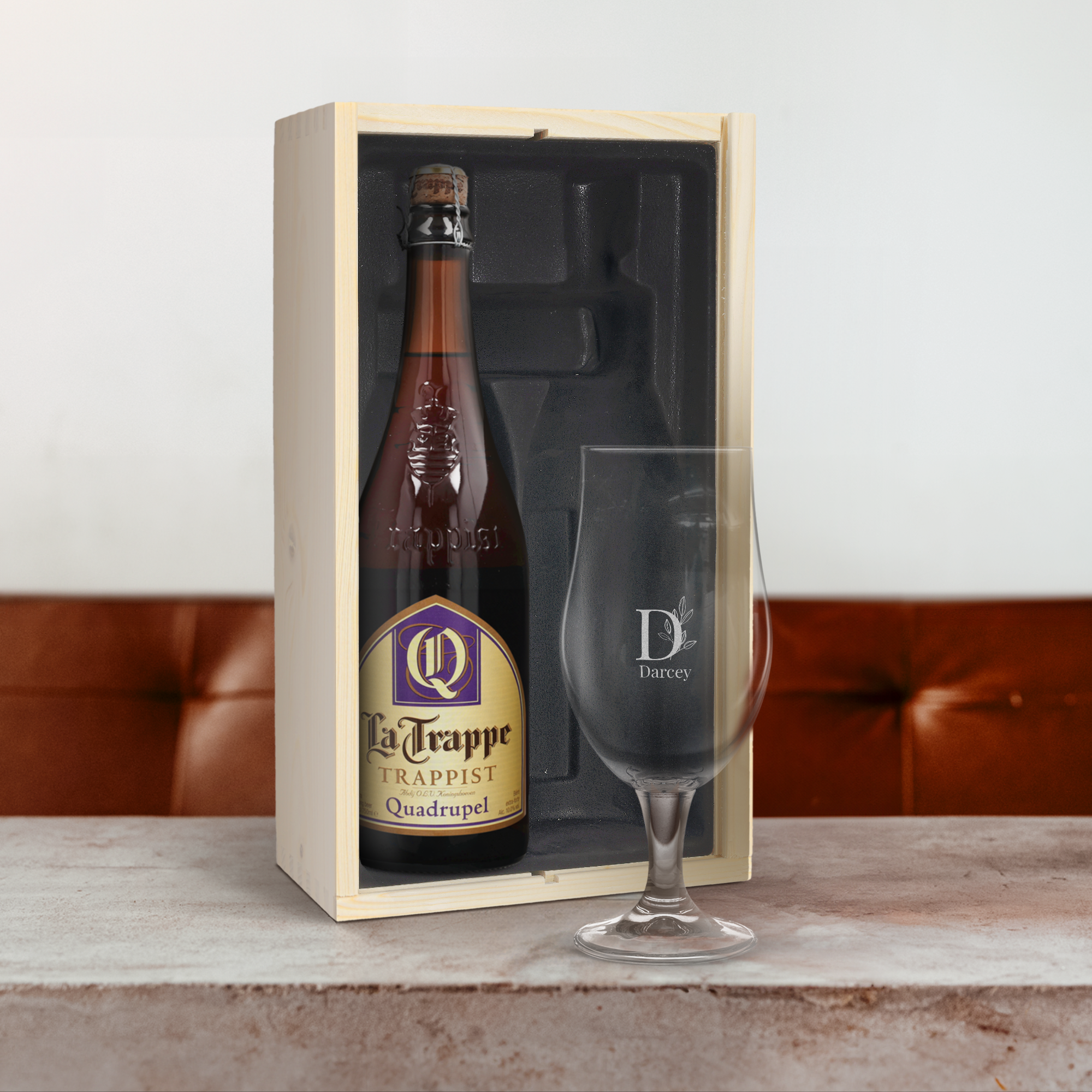 Set de regalo de cerveza con vidrio grabado con el nombre "Darcey" y la inicial "D" dentro de un diseño floral, junto a una botella La Trappe en caja de madera.
