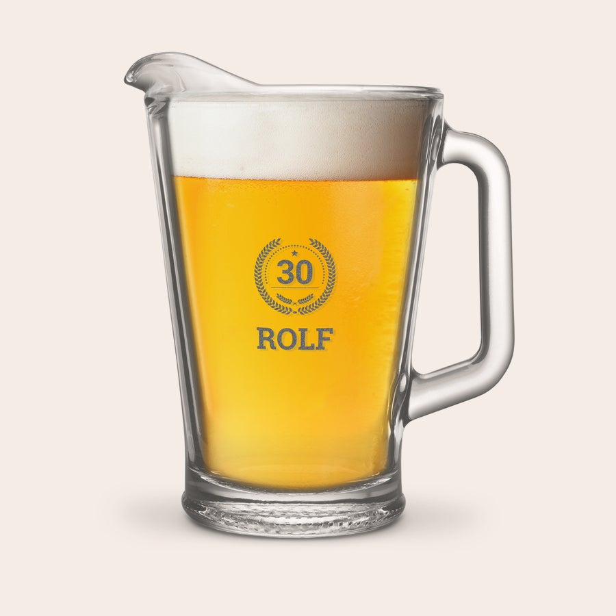 Glaskrug mit Gravur Glaskrug mit Bier gefüllt, personalisiert mit gravierter Zahl 30 und dem Namen ROLF, umrandet von einem Lorbeerkranz