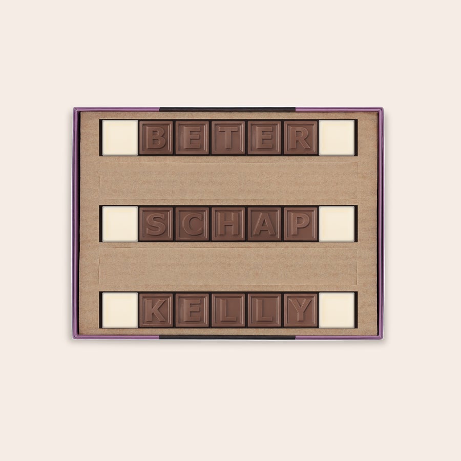 Chocotelegram Gepersonaliseerd chocotelegram met de boodschap "BETER SCHAP KELLY" gemaakt van melk- en witte chocolade blokjes, gepresenteerd in een cadeauverpakking.