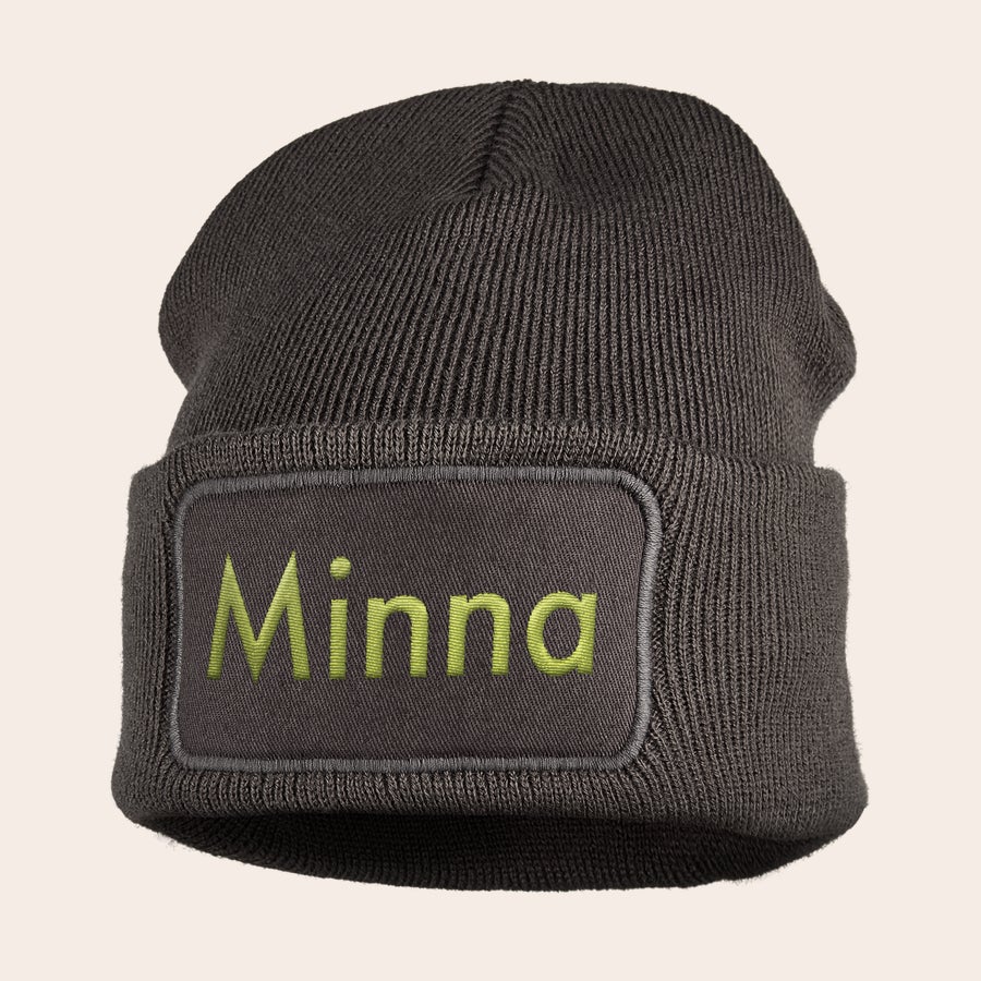 Pipo nimellä - Brodeeraus Ruskea pipo, jossa on brodeerattu vihreä nimi Minna harmaassa nimikyltissä pitää korvasi lämpiminä