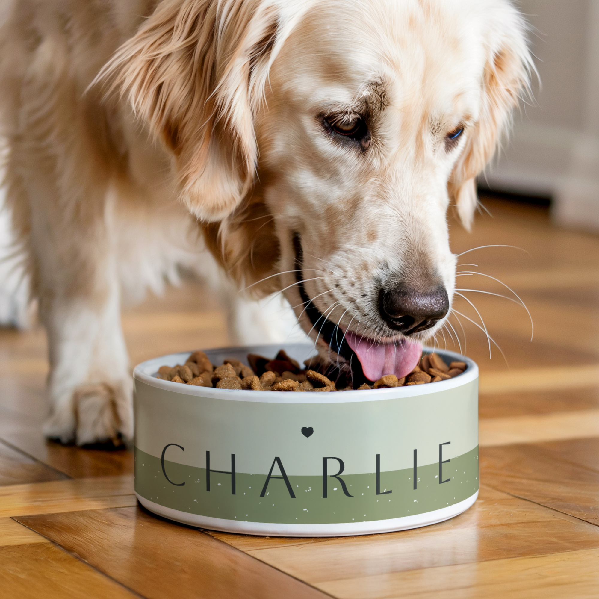 A golden retriever eating from a personalized ceramic pet food bowl with the printed name Charlie and a heart icon