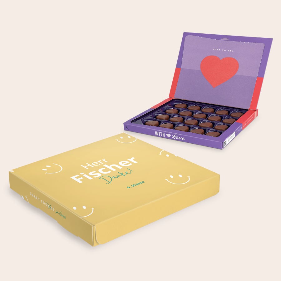Pralinen Milka Lehrer Personalisierte Milka-Geschenkbox für Lehrer, bedruckt mit dem Namen "Herr Fischer Danke" und "4. Klasse" auf gelbem Hintergrund. Die offene Box zeigt herzförmige Pralinen und die Aufschrift "JUST TO SAY WITH LOVE" mit einem roten Herz.
