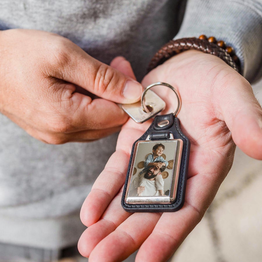 Porta-chaves de couro com foto Chaveiro de couro com foto impressa de pai e filho, segurado por uma mão. Surpreenda com um chaveiro de couro com a sua foto!