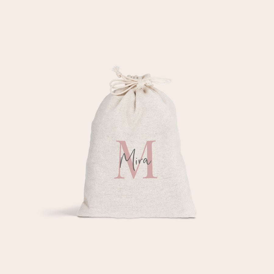 Presentpåse med dragsko Ljus personlig presentpåse med dragsko, tryckt med en rosa stor bokstav M och namnet Mira över. Gör påsken speciell med personliga presentpåsar med dragsko.