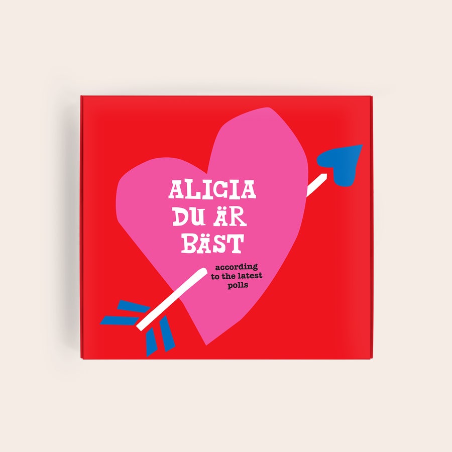 Tony's Chocolonely Presentask Tony's Chocolonely mjölkchoklad i personlig presentförpackning med texten ALICIA DU ÄR BÄST enligt de senaste undersökningarna på ett rosa hjärta genomborrat av en vit pil med blå fjädrar mot röd bakgrund.