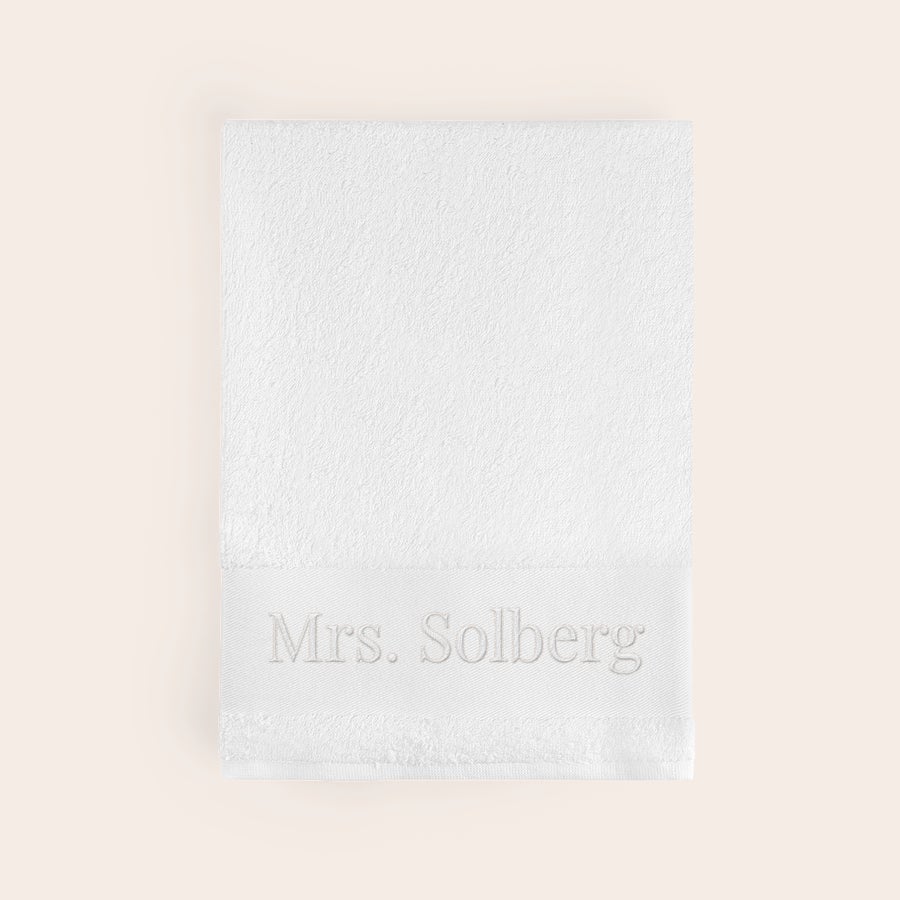 Håndkle med tekst Hvit, supermyk håndkle brodert med "Mrs. Solberg" i lysegrå tråd. Få dette supermyke og kosete håndkleet brodert med navn!