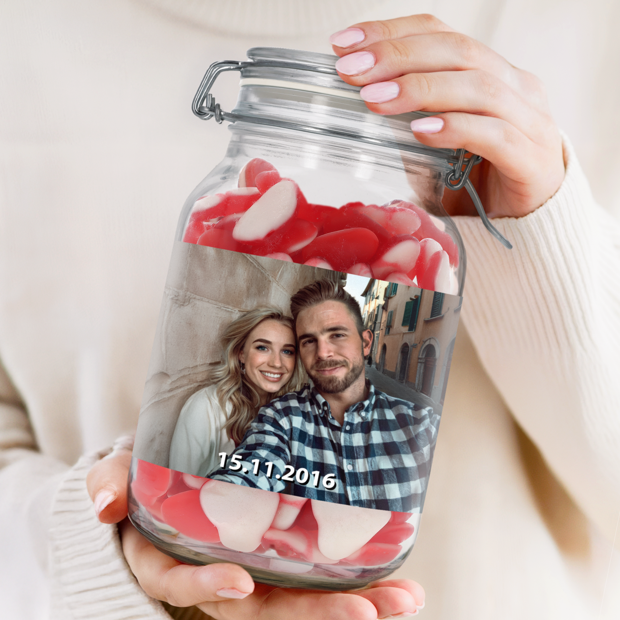 Hands holding a personalised sweet jar with heart-shaped candies, printed with a photo of a couple and a date.
