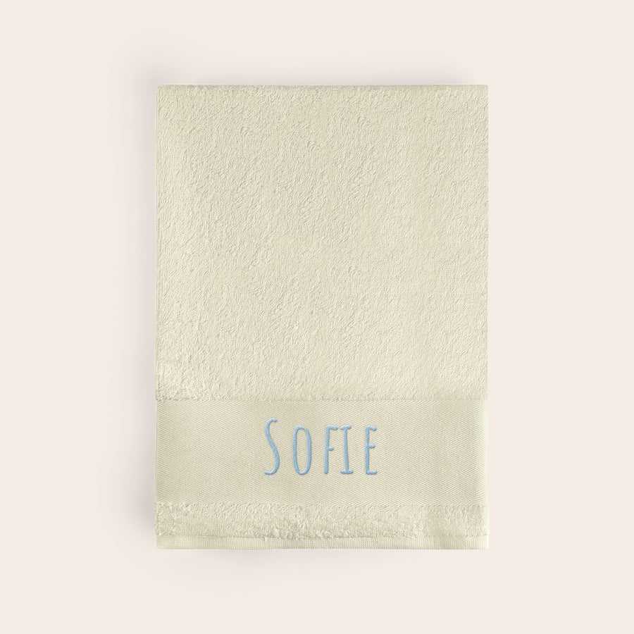 Badehåndklæde med tekst Beige super blødt strand håndklæde med navnet "SOFIE" broderet i lyseblå.