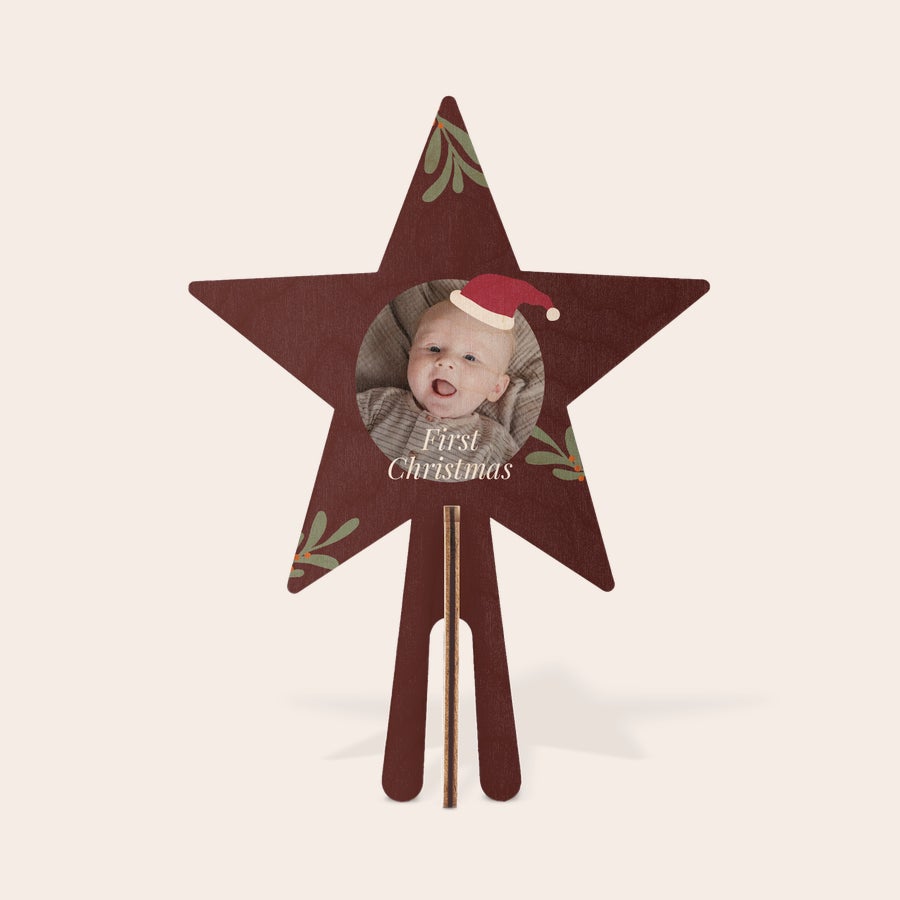 Konstgjord julgran med personlig stjärntopp i trä Rödbrun personlig trätopp med tryckt bild av ett barn i tomteluva och texten First Christmas, dekorerad med mistelkvistar. Topp för återanvändbar minijulgran.