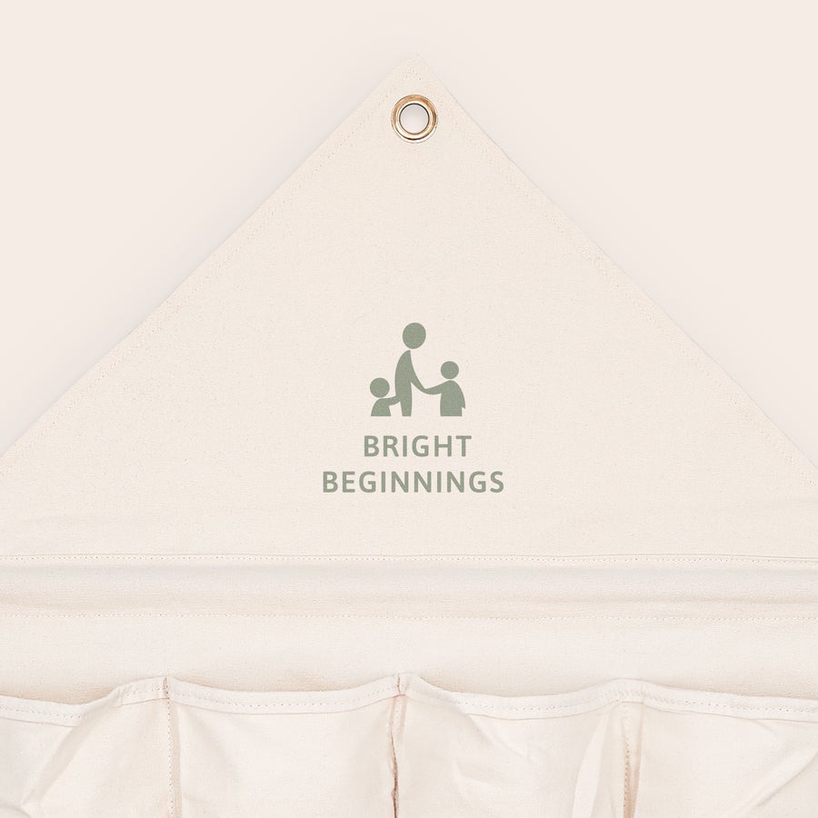 Závěsný organizér se jménem a/nebo fotografií Bílý personalizovaný kapesní organizér s nápisem BRIGHT BEGINNINGS a dětskými motivy, s praktickým závěsným systémem.
